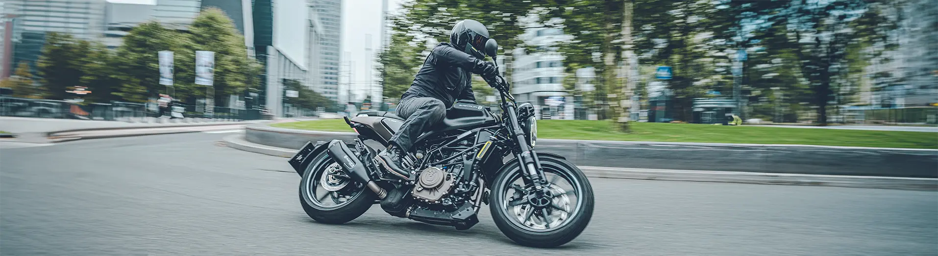 A Husqvarna Norden 901 Expedition rider is riding on a winding road with a forest in the background